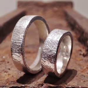 May include: Two silver wedding bands with a textured finish. The bands are stacked on top of each other.