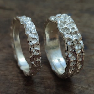 May include: Two silver rings with a textured, organic design. The rings are both wide and have a rough, hammered finish.