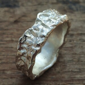 May include: A silver ring with a textured, organic design. The ring is made of a smooth, polished metal and has a unique, irregular shape.