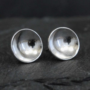 May include: A pair of silver stud earrings with a rounded, slightly concave design.