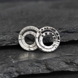 May include: A pair of silver earrings with a hammered finish. Each earring features two concentric circles.