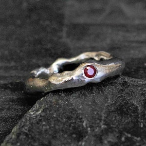 Può includere: Un anello d'argento con una fascia testurizzata e una singola pietra preziosa rossa.