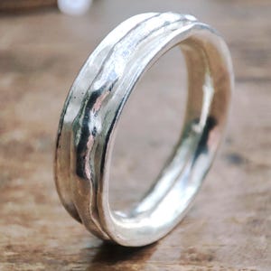 May include: A silver ring with a textured, wavy design. The ring has a polished, reflective surface, and the design appears to be a continuous, flowing pattern. The ring is a piece of jewelry.