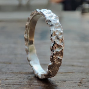 May include: A silver ring with a textured, organic design. The ring is made of metal and has a smooth, polished finish.