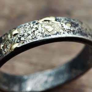 May include: A silver band with a textured surface and small gold accents.