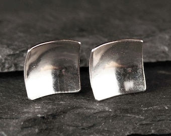 May include: A pair of silver square-shaped earrings with a slightly curved surface.