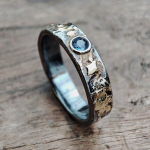 May include: A silver ring with a textured band and a small blue gemstone set in gold.