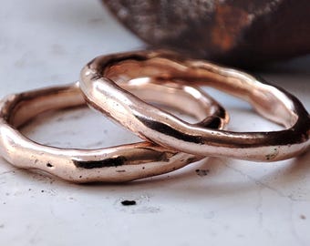 Op de afbeelding: Twee roségouden ringen met een textuur, organisch ontwerp. De ringen zijn op elkaar gestapeld en tonen hun unieke, onregelmatige vorm en warme metaalkleur. De achtergrond is wazig en neutraal.
