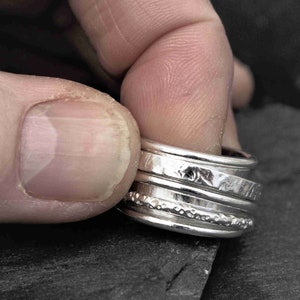 May include: A set of four silver stacking rings with different textures and patterns. The rings are worn on a finger.