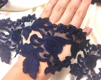 May include: A length of dark navy blue lace trim featuring an intricate floral and leaf embroidery pattern on a sheer mesh background. The lace has a scalloped edge and a continuous design, showcasing detailed stitching and a deep blue color palette.