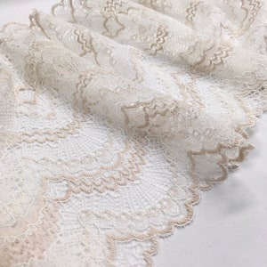 May include: Close-up of a delicate, off-white lace fabric with a scalloped edge. The lace features intricate floral patterns and a subtle beige trim, creating a soft, textured appearance. The fabric is draped, showcasing its flexibility and design.