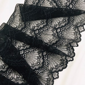 May include: Close-up of black lace fabric with a detailed, openwork design. The lace is folded, revealing layers of the intricate pattern. The fabric's delicate texture and dark colour create a striking visual contrast against the white background.