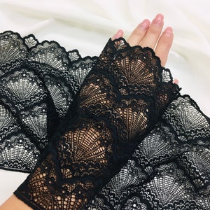 May include: Black lace fabric with a delicate, openwork design. The lace features a scalloped edge and a fan-like pattern. The fabric is displayed against a white background, highlighting the intricate details of the lace.