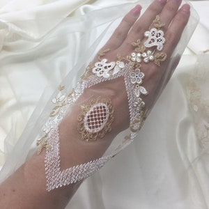 May include: Ivory bridal veil with detailed gold and white floral and geometric embroidery. The delicate lace design includes a diamond pattern and an oval medallion, ideal for weddings and special events. The veil is made of a sheer fabric.