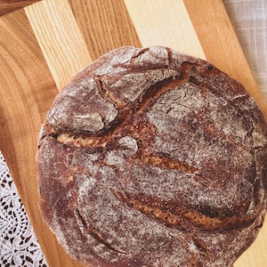 May include: A round loaf of dark brown bread with a slightly cracked crust, sitting on a wooden cutting board.