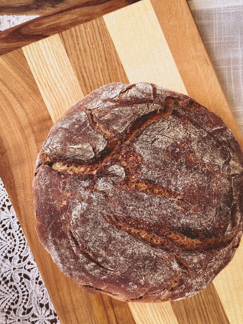 May include: A round loaf of dark brown bread with a slightly cracked crust, sitting on a wooden cutting board.