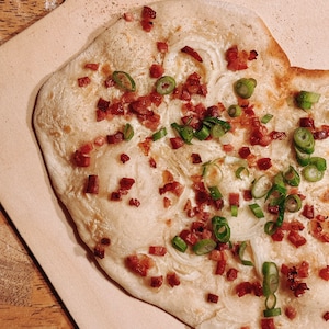 May include: A flatbread topped with bacon, onions, and green onions. The flatbread is cooked until golden brown and the toppings are evenly distributed.