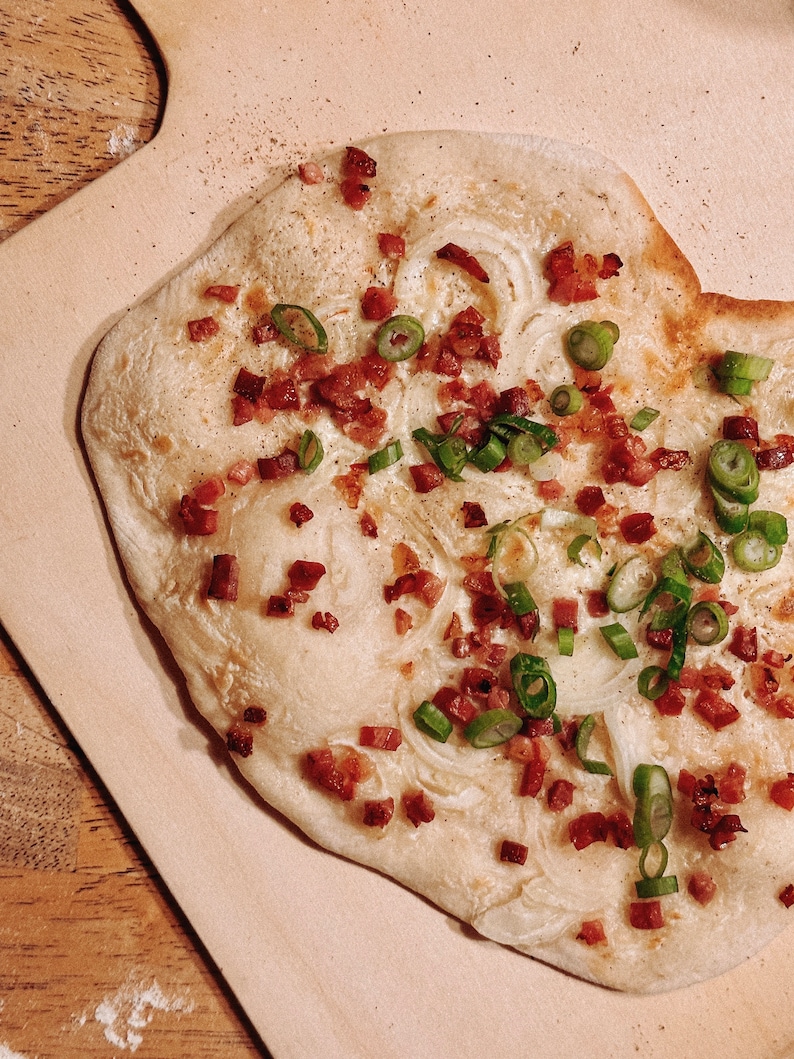 May include: A flatbread topped with bacon, onions, and green onions. The flatbread is cooked until golden brown and the toppings are evenly distributed.