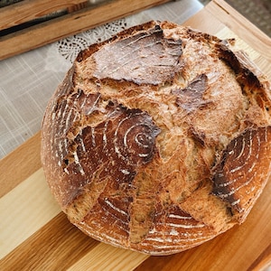 May include: A freshly baked loaf of sourdough bread with a crispy crust and a deep brown color. The bread has a distinctive pattern of swirls and cracks on the surface.