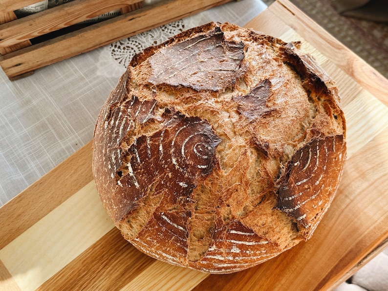May include: A freshly baked loaf of sourdough bread with a crispy crust and a deep brown color. The bread has a distinctive pattern of swirls and cracks on the surface.