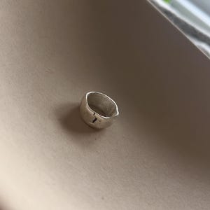 May include: A silver ring with a textured, irregular shape. The ring has a small, vertical line etched into the surface.