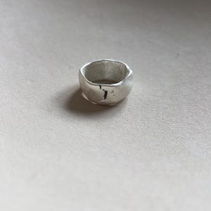 May include: A silver ring with a textured, irregular shape. The ring has a slightly hammered finish.