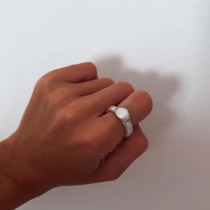 Puede incluir: Un anillo de plata con una parte superior ovalada texturizada.