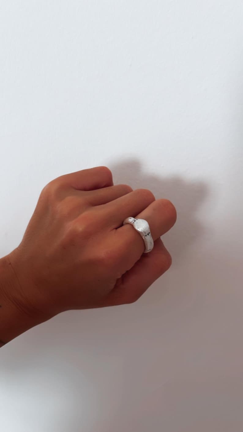 Puede incluir: Un anillo de plata con una parte superior ovalada texturizada.