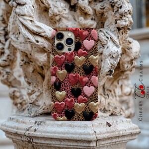 May include: A phone case with a pink, gold, and black heart pattern. The case is designed for an iPhone with a triple lens camera.