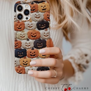 Puede incluir: Una funda blanca para iPhone con un patr&oacute;n de caras de calabaza naranja, blanca y negra. La funda est&aacute; dise&ntilde;ada para un iPhone 13 Pro Max.