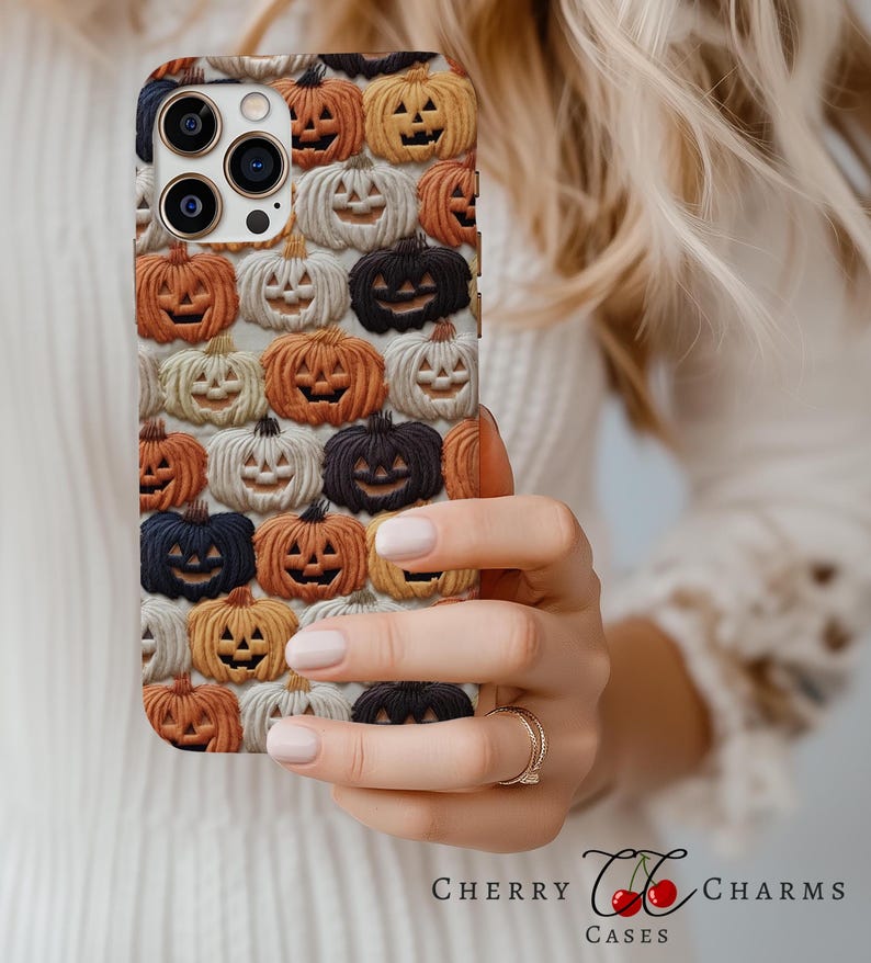 Puede incluir: Una funda blanca para iPhone con un patr&oacute;n de caras de calabaza naranja, blanca y negra. La funda est&aacute; dise&ntilde;ada para un iPhone 13 Pro Max.