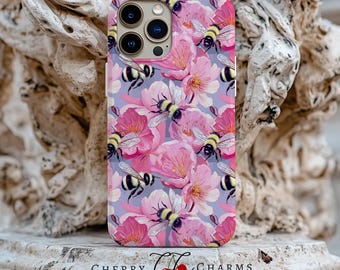 Puede incluir: Una funda para teléfono con un diseño floral con flores rosas y abejas. La funda tiene un recorte para la cámara y una parte posterior transparente.