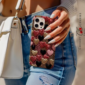 May include: A pink, black, and gold phone case with a heart pattern. The case is made of a durable material and has a sleek design.