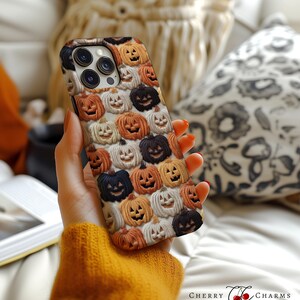 Puede incluir: Una funda negra para iPhone con un patr&oacute;n de caras de calabaza naranja y blanca. La funda se est&aacute; sosteniendo en una mano.