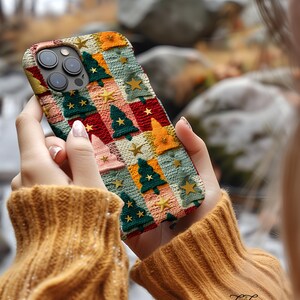 Op de afbeelding: Een kleurrijke telefoonhoes met een gebreid patroon met kerstboommotieven en sterren. De hoes is gemaakt van zacht, flexibel materiaal en heeft een verhoogde rand om het scherm te beschermen.