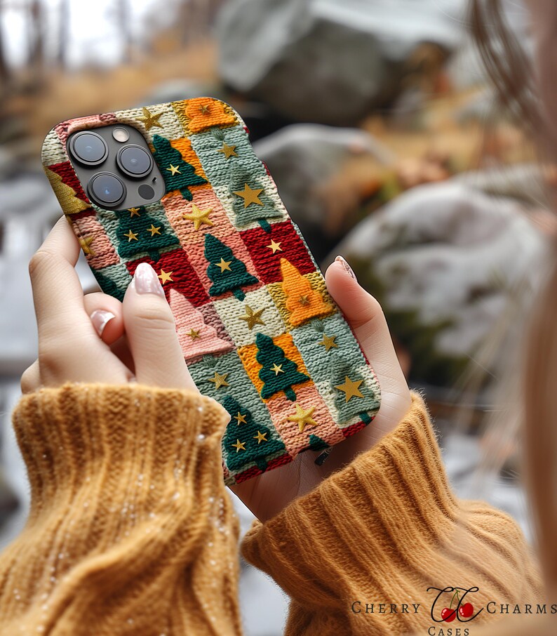Op de afbeelding: Een kleurrijke telefoonhoes met een gebreid patroon met kerstboommotieven en sterren. De hoes is gemaakt van zacht, flexibel materiaal en heeft een verhoogde rand om het scherm te beschermen.