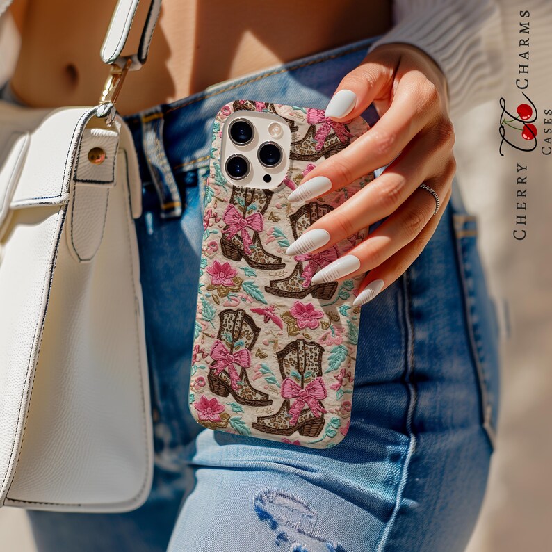 May include: A white iPhone case featuring a pattern of pink bows and brown cowboy boots. The case has a camera lens cutout and a white background.