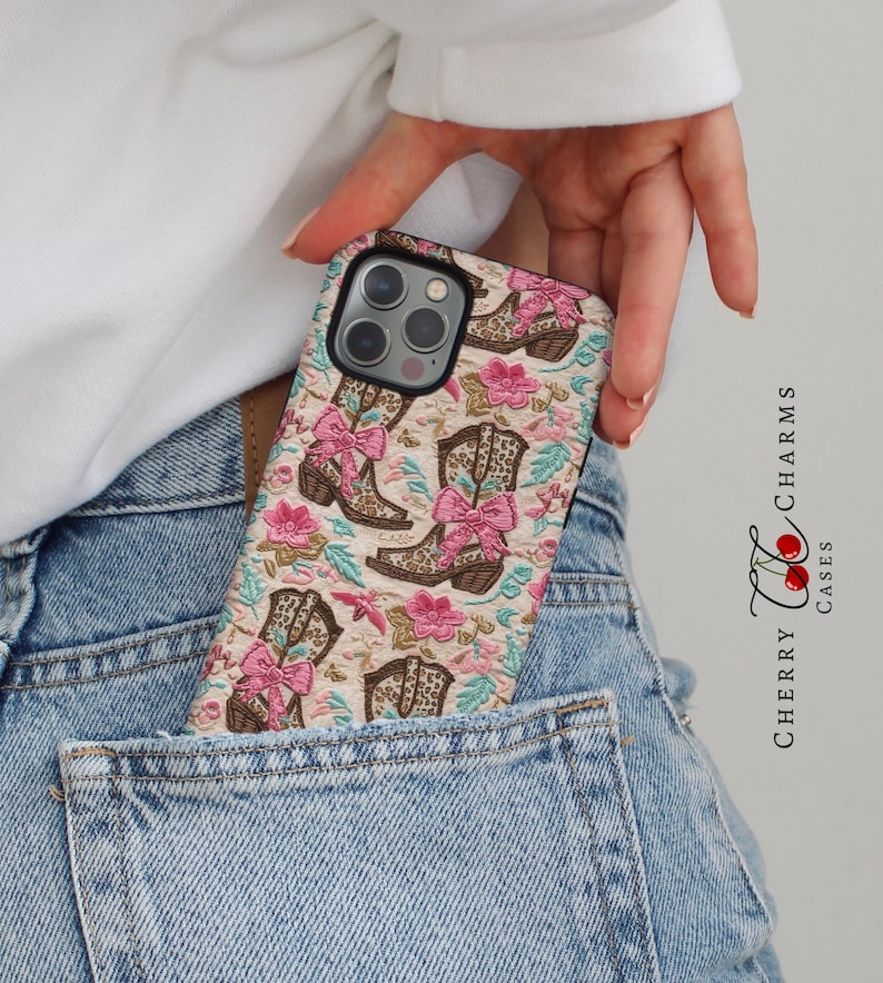 May include: A phone case with a beige background and a pattern of brown cowboy boots with pink bows and floral accents. The case is in a back pocket of blue jeans.