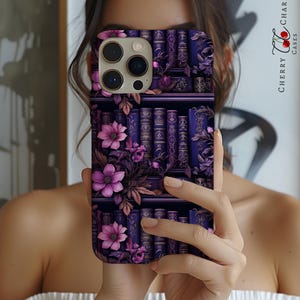 Może przedstawiać: Fioletowe etui na telefon z kwiatowym wzorem i regałem z książkami. Etui ma wycięcie na obiektyw aparatu.