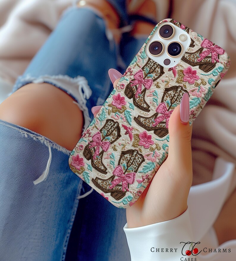 May include: A white phone case featuring a pattern of pink bows and brown cowboy boots. The case has a camera lens cutout and a floral design.