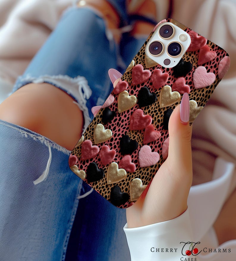 May include: A phone case with a pink, black, and gold heart pattern on a leopard print background. The case has a raised lip around the camera lens.