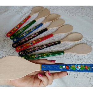 May include: Wooden kitchen utensils with painted handles. The handles are decorated with floral patterns in various colors, including red, green, blue, and black. One spatula has a blue handle with the word "UKRAINE".