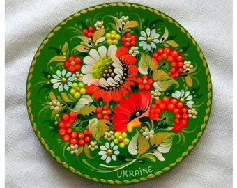 May include: A green round plate with a painted floral design. The flowers are red, orange, white, and yellow. The plate has a gold rim and the word "UKRAINE" is written on the bottom.