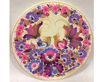 May include: A round wooden plate painted with a floral design featuring two birds with colorful plumage. The plate is decorated with pink, purple, blue, and gold flowers and leaves. The text "UKRAINE" is written in the bottom right corner of the plate.