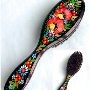 以下が含まれることがあります： 黒いハンドルと天然毛のブラシヘッドが付いた木製ヘアブラシ。ハンドルには赤、青、緑、金色の花柄が描かれています。