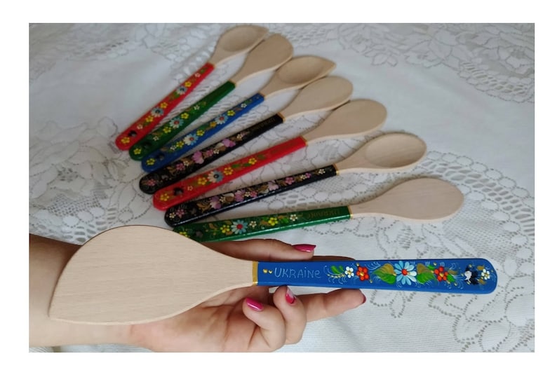 May include: Wooden kitchen utensils with painted handles. The handles are decorated with floral patterns in various colors, including red, green, blue, and black. One spatula has a blue handle with the word "UKRAINE".