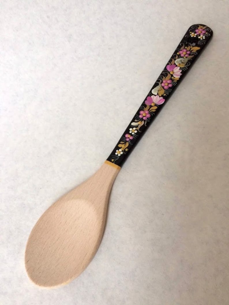 May include: Wooden spoon with a light-colored, oval-shaped bowl and a long, black handle. The handle is decorated with a floral pattern in pink, white, and yellow. The spoon is likely used for cooking and serving.