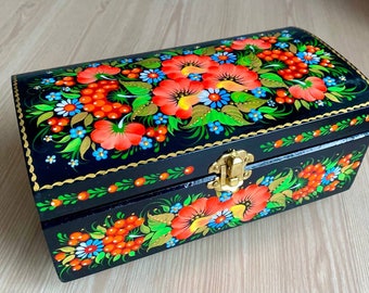 May include: A black wooden box with a hinged lid decorated with hand-painted floral designs in red, orange, green, blue, and gold. The box has a brass latch.