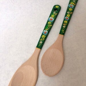 May include: Two wooden kitchen utensils: a spatula and a spoon. The handles are painted green and decorated with colorful floral patterns. The spatula is approximately 12 inches long, and the spoon is about 11 inches long.
