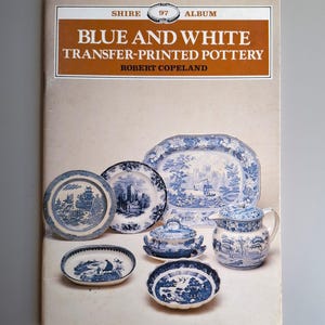 May include: A book cover titled "Blue and White Transfer-Printed Pottery" by Robert Copeland. The image displays an assortment of blue and white transferware pottery, including plates, a serving dish, and a jug.